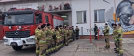 Zdjęcie przedstawia strażaków na tle remizy podczas odprawy przed ćwiczeniami