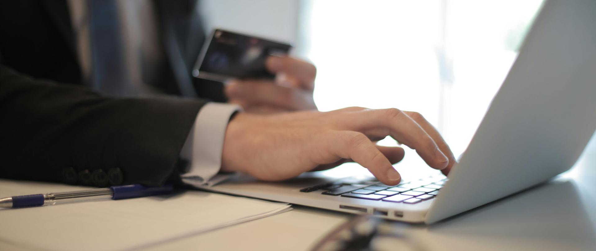 Mężczyzna w czarnym garniturze pisze na klawiaturze laptopa