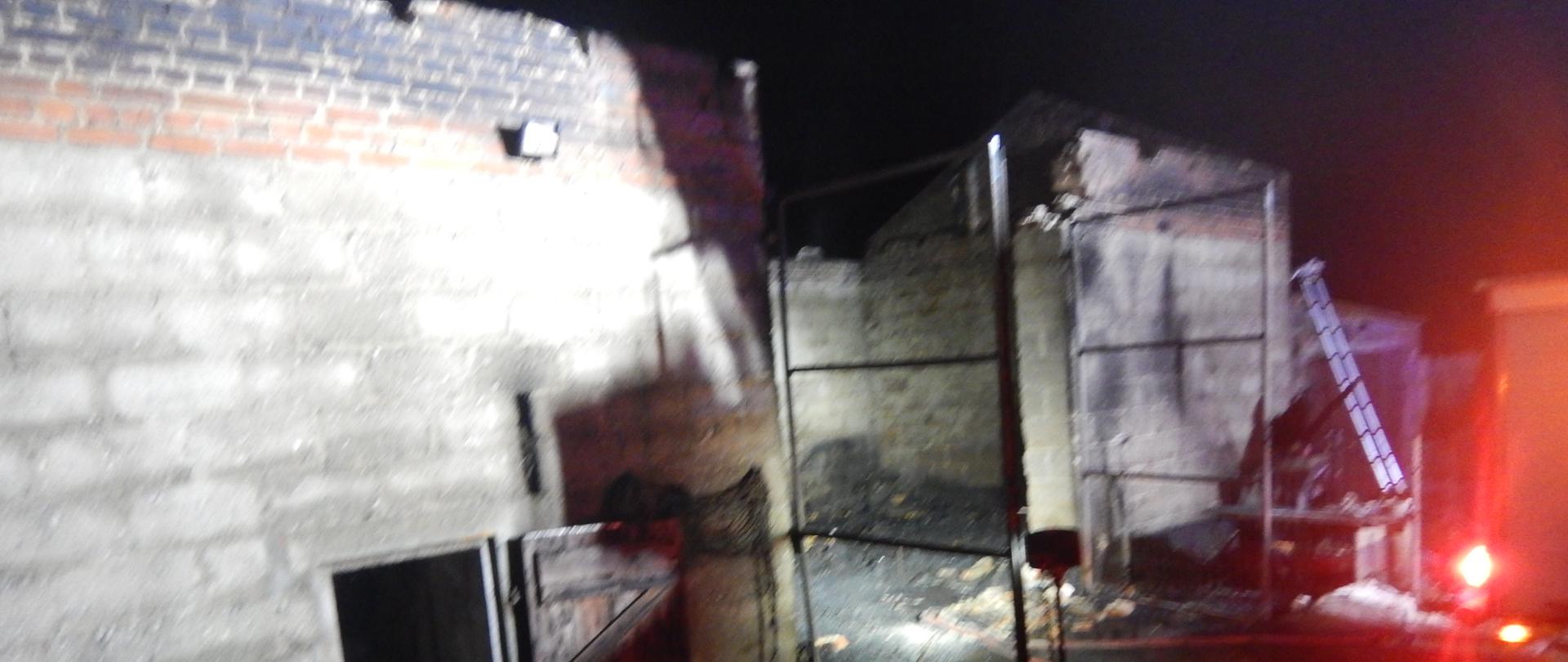 Zdjęcie przedstawia spalony budynek stodoły. Obok obiektu znajduje się rusztowanie oraz nadpalone elementy konstrukcji dachu.