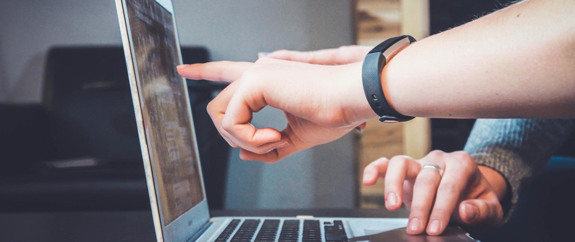 Ręce wskazujące ekran laptopa.