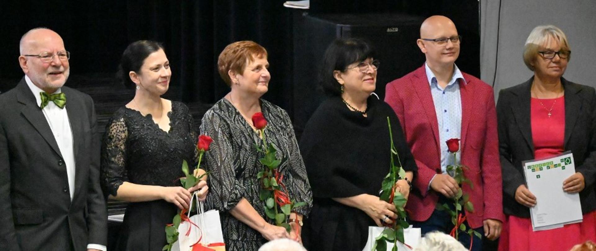 Zdjęcie kolorowe. Sześć osób, cztery z nich trzymają czerwone róże