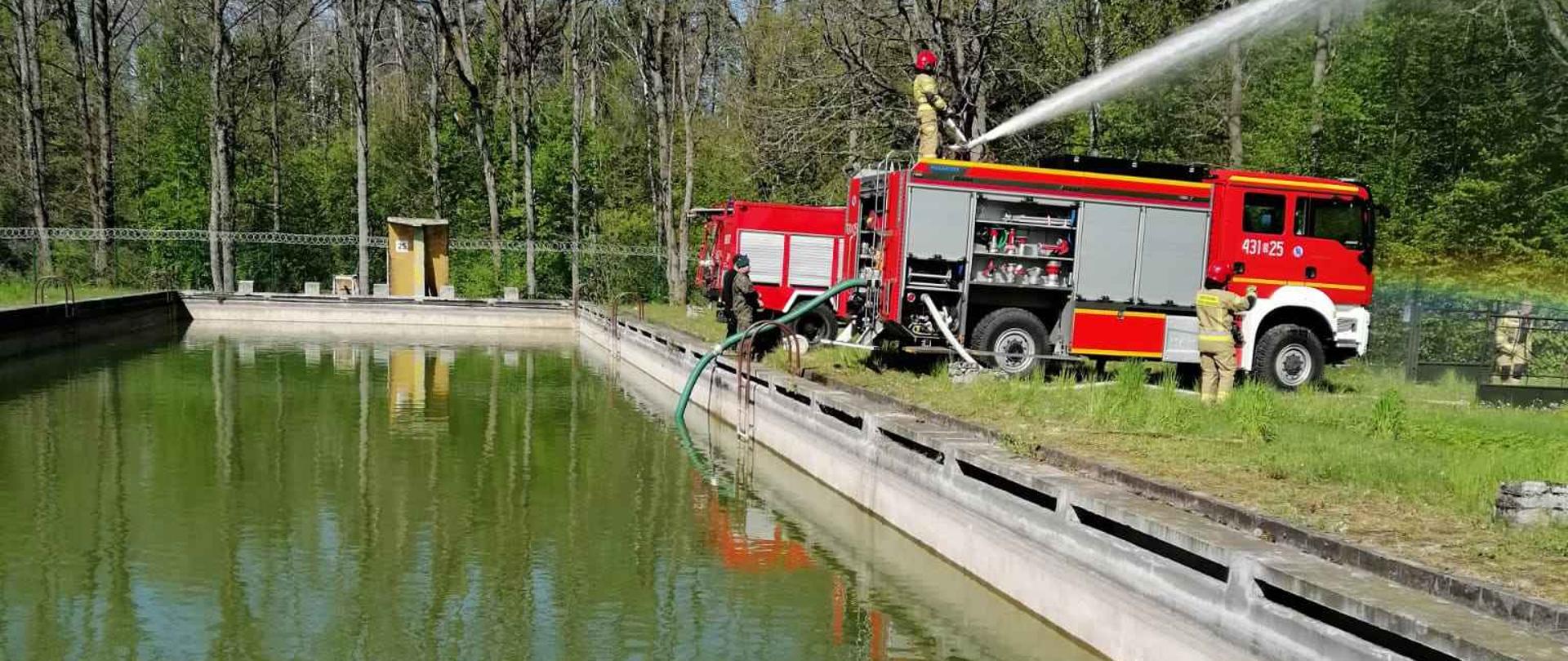 Strażacki wóz bojowy zasysa wodę z basenu i podaje działkiem na dachu.