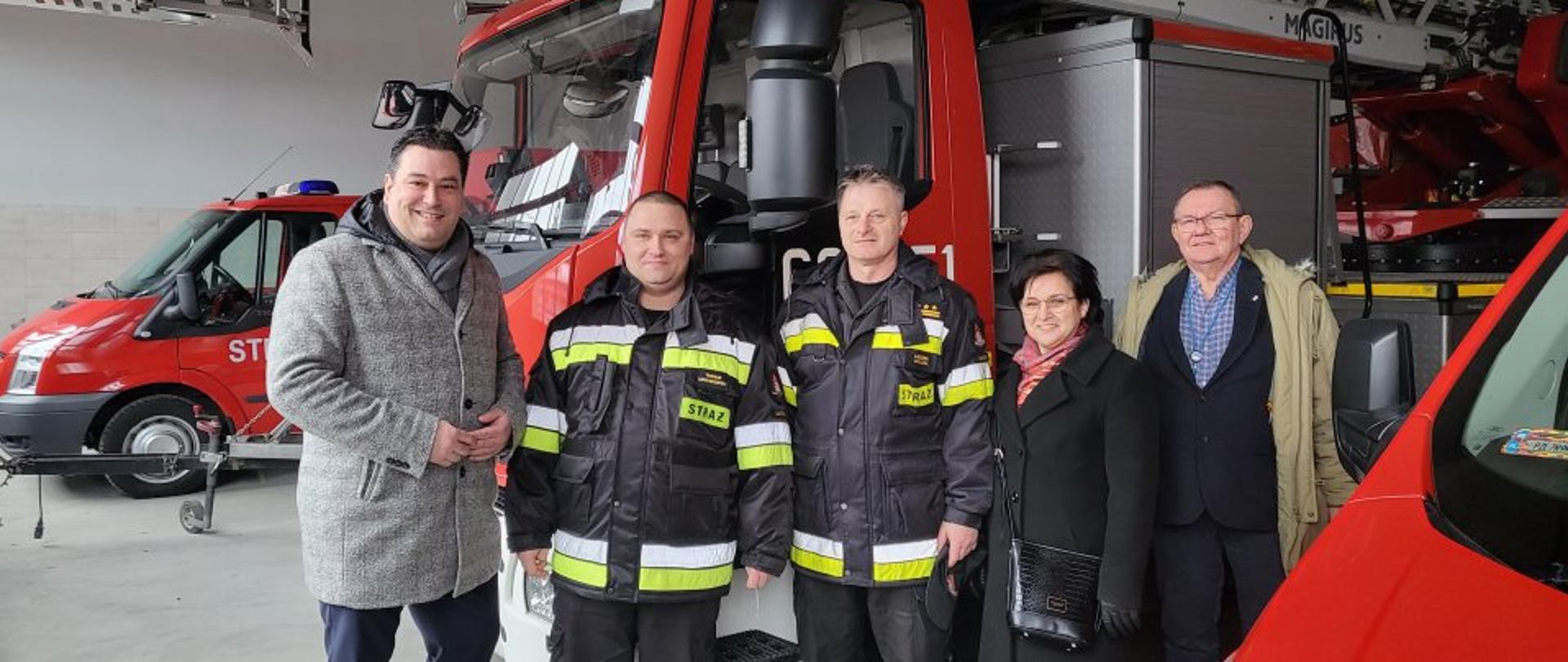 na zdjęciu przed samochodem strażackim stoją osoby