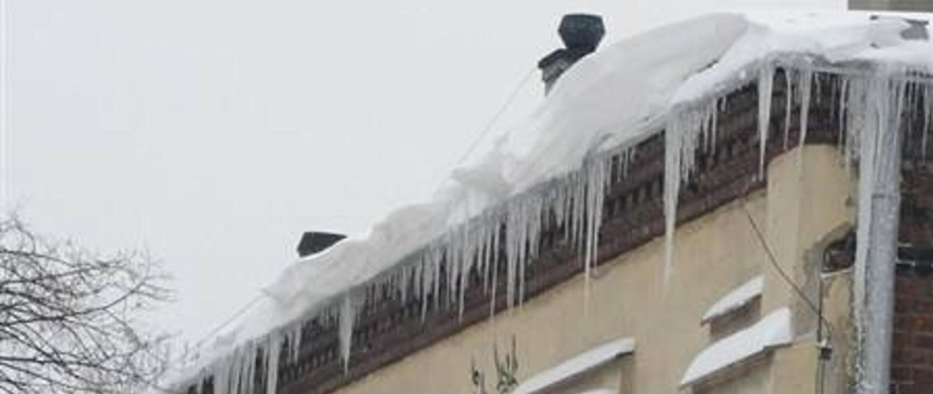 Zdjęcie przedstawia zalegający śnieg i nawisów lodowych na dachu budynku