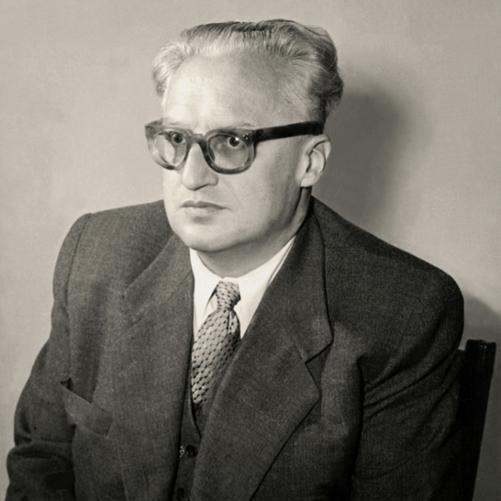 Stanisław Skrzeszewski - czarno-biały portret mężczyzny w okularach z grubymi oprawkami, siwe włosy, ciemna marynarka, jasny krawat w drobne ciemne wzory, kamizelka.