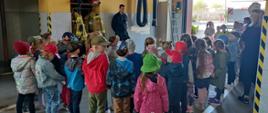 Dzieci z przedszkola podczas spotkania ze strażakami w garażu oglądają prezentację sprzętu strażackiego i wyposażenia
