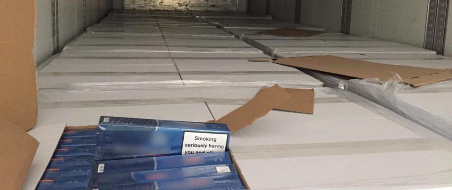 Wnętrze naczepy, rozerwany karton, z którego wystają paczki papierosów.