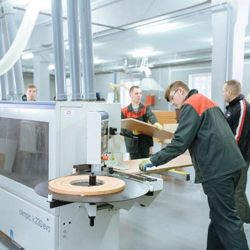 Trzech chłopców pod nadzorem nauczyciela pracują w zakładzie stolarskim