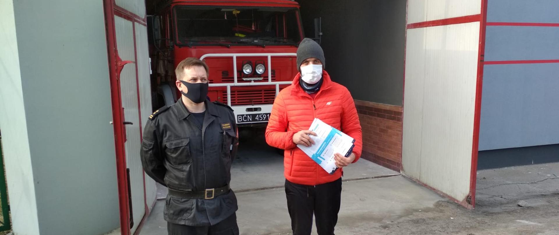zdjęcie przedstawia funkcjonariusza KP PSP w Żninie przekazującego pakiet ulotek promujących akcje szczepień przeciwko Covid-19 