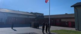 Funkcjonariusze Komendy Powiatowej Państwowej Straży Pożarnej w Rypinie, wraz z dowódcą jednostki ratowniczo-gaśniczej znajdują się na placu jednostki i oddają hołd w kierunku flagi polski która została wciągnięta na maszt przez poczet flagowy.