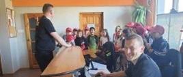 KP PSP w Białogardzie - wizyta dzieci i młodzieży z białogardzkich szkół w ramach akcji” Bezpieczne Wakacje”. Zdjęcie przedstawia Stanowisko Kierowania i strażaka omawiającego pracę dyspozytora w obecności dzieci
