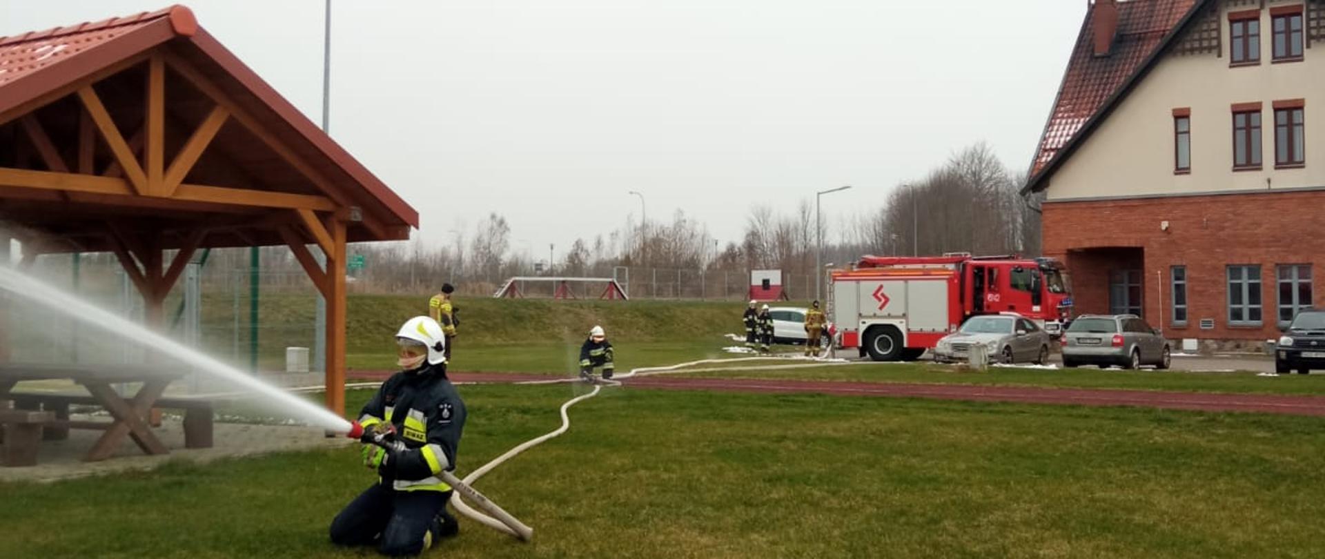 Zdjęcie przedstawia jeden z elementów egzaminu praktycznego szkolenia podstawowego strażaka ratownika Ochotniczych Straży Pożarnych, realizowanego w Komedzie Powiatowej Państwowej Straży Pożarnej w Gołdapi, polegającego na weryfikacji umiejętności i znajomości w zakresie prowadzenia działań gaśniczych 