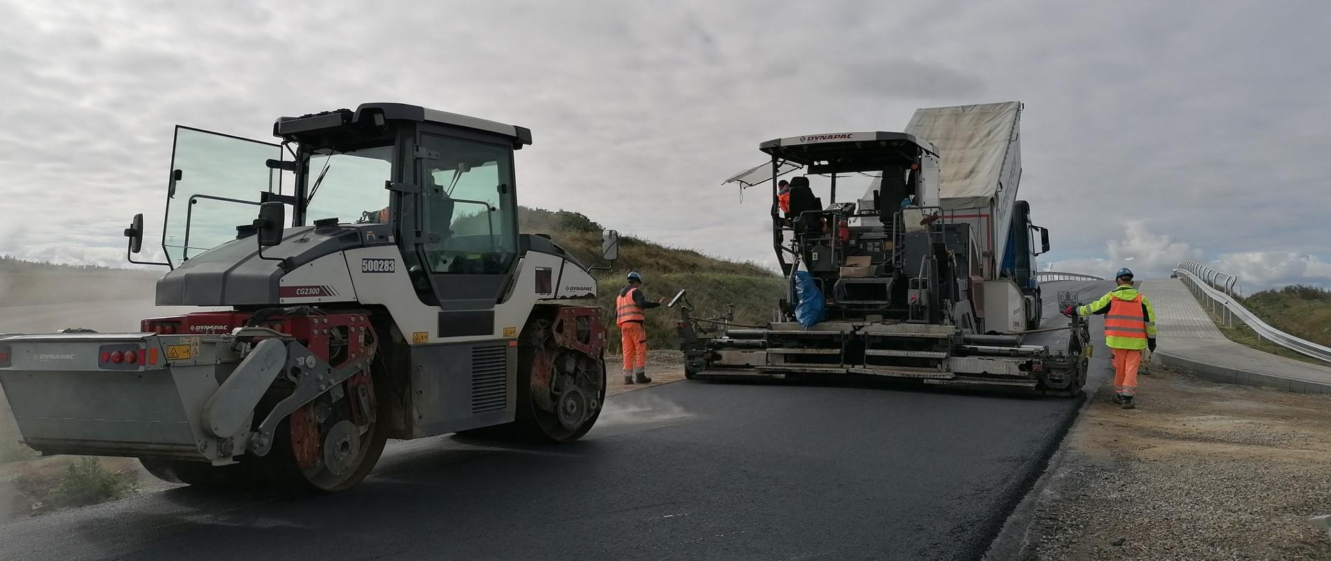 Łącznik północny do obwodnicy Opatowa - układanie nawierzchni na wiadukcie, wlec drogowy, rozściełacz do asfaltu, dwóch pracowników obok maszyny