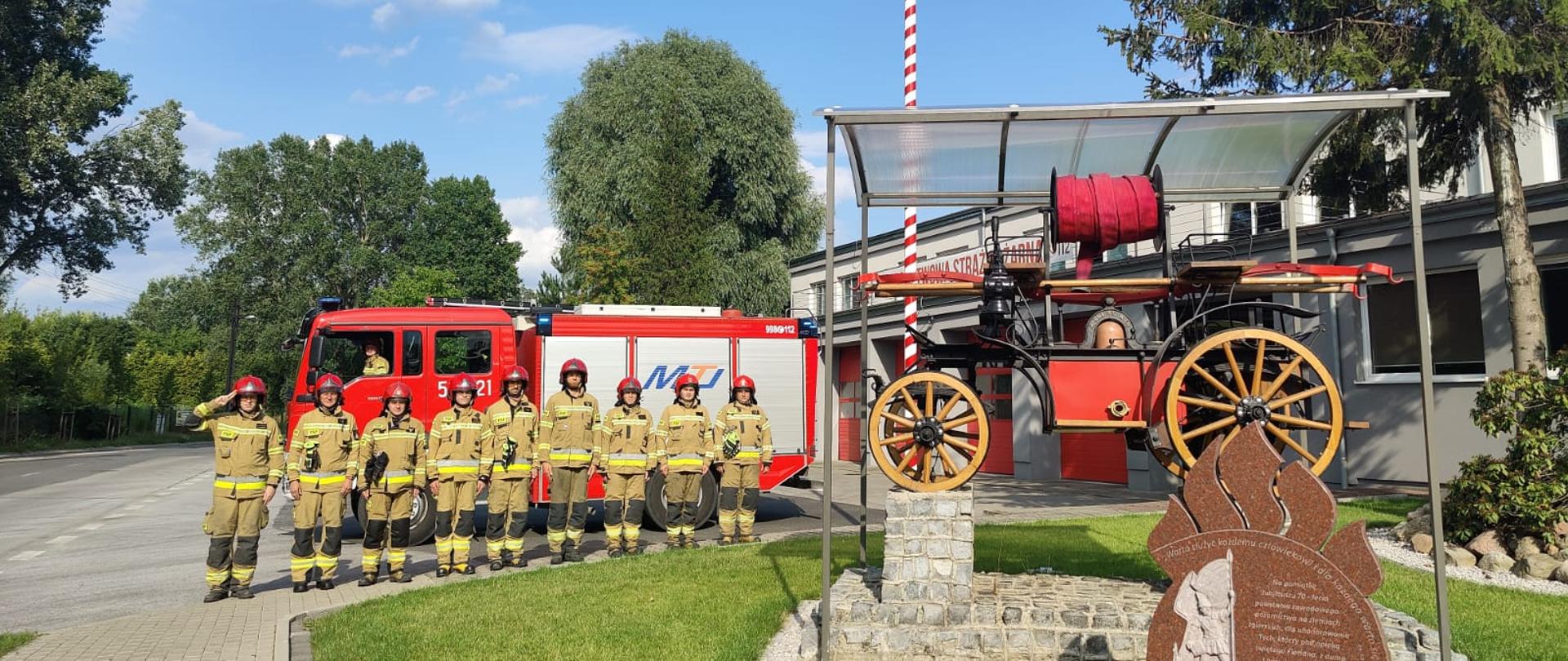 Zdjęcie przedstawia strażaków stojących w szeregu na tle JRG Zgierz.