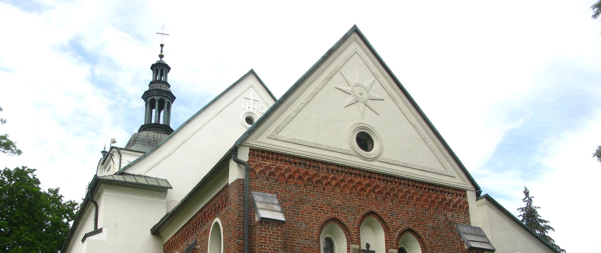 Zdjęcia przedstawia kościół św. Mikołaja w Sławkowie, otoczony drzewami, zdjęcie wykonane od strony prezbiterium. Z przodu kościoła wieżą zwieńczona krzyżem, dach pokryty blachą miedzianą, prezbiterium kościoła z cegły, reszta otynkowana. 