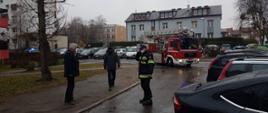 Samochód strażacki wjeżdża na osiedle przed nim stoi strażak oraz dwie osoby