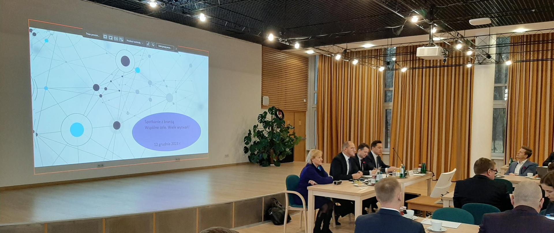 Sala Zespołu organizacji spotkań i konferencji GDDKiA w Józefowie. Ok. 200 osób zebranych przy stołach dyskutuje o tematach związanych z branżą budowlaną.