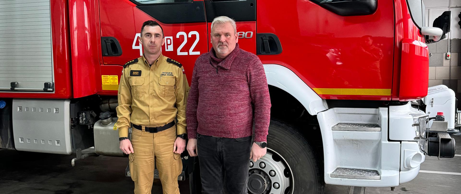 Komendant powiatowy PSP oraz prezes OSP stoją w garaży JRG. W tle samochód pożarniczy, na podłodze leżą aparaty.