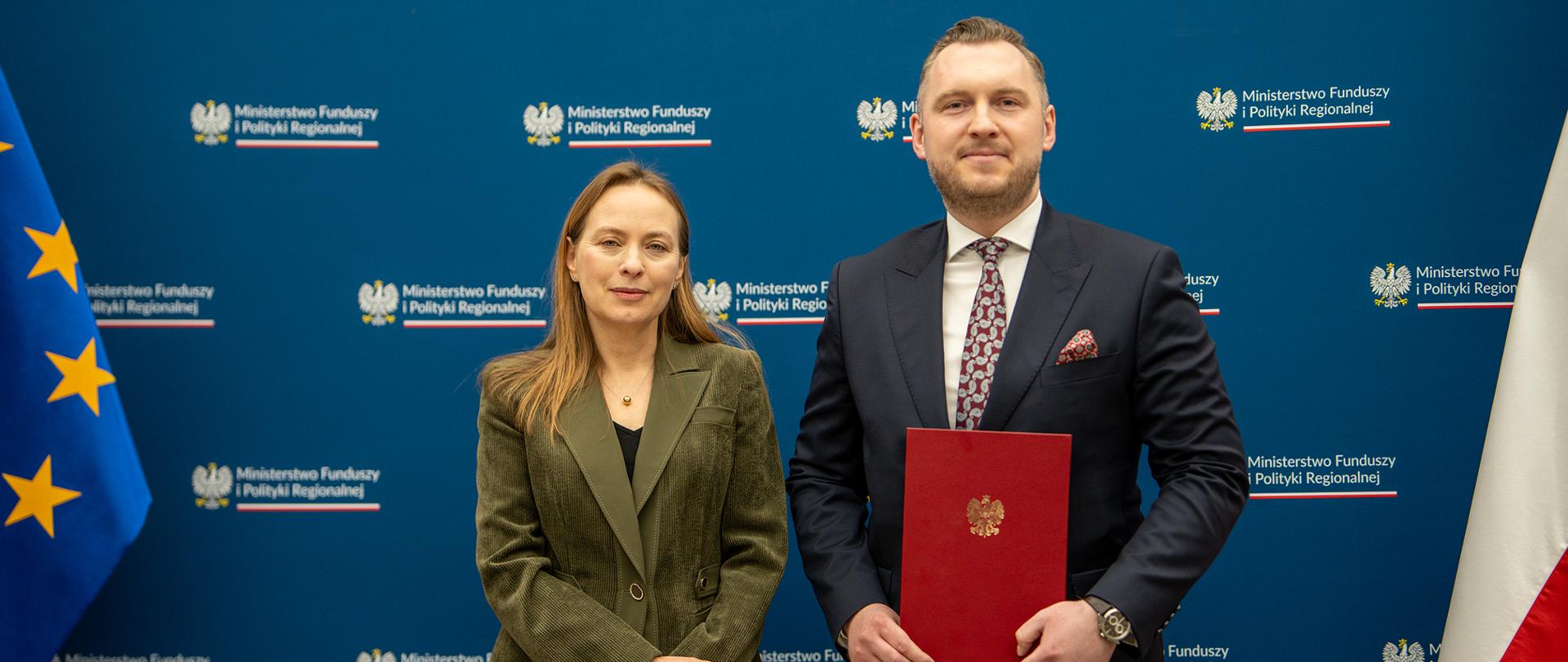 Minister funduszy i polityki regionalnej Katarzyna Pełczyńska-Nałęcz wręcza powołanie na wiceministra Konradowi Wojnarowskiemu, stoją na tle ścianki