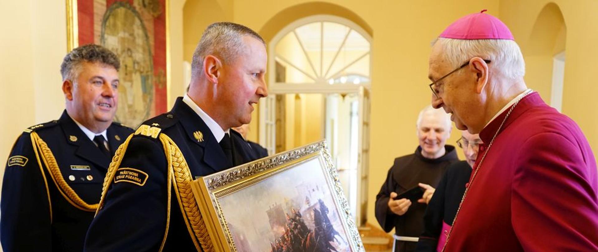 strażak przekazuje obraz pamiątkowy arcybiskupowi Gądeckiemu