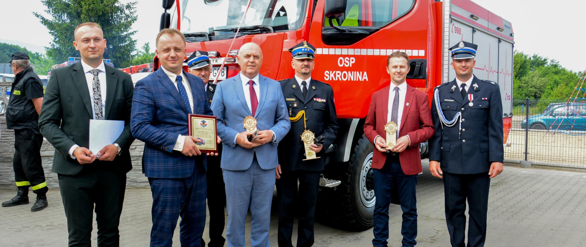 druhowie, strażacy i politycy pozują do zdjęcia na tle samochodu gaśniczego