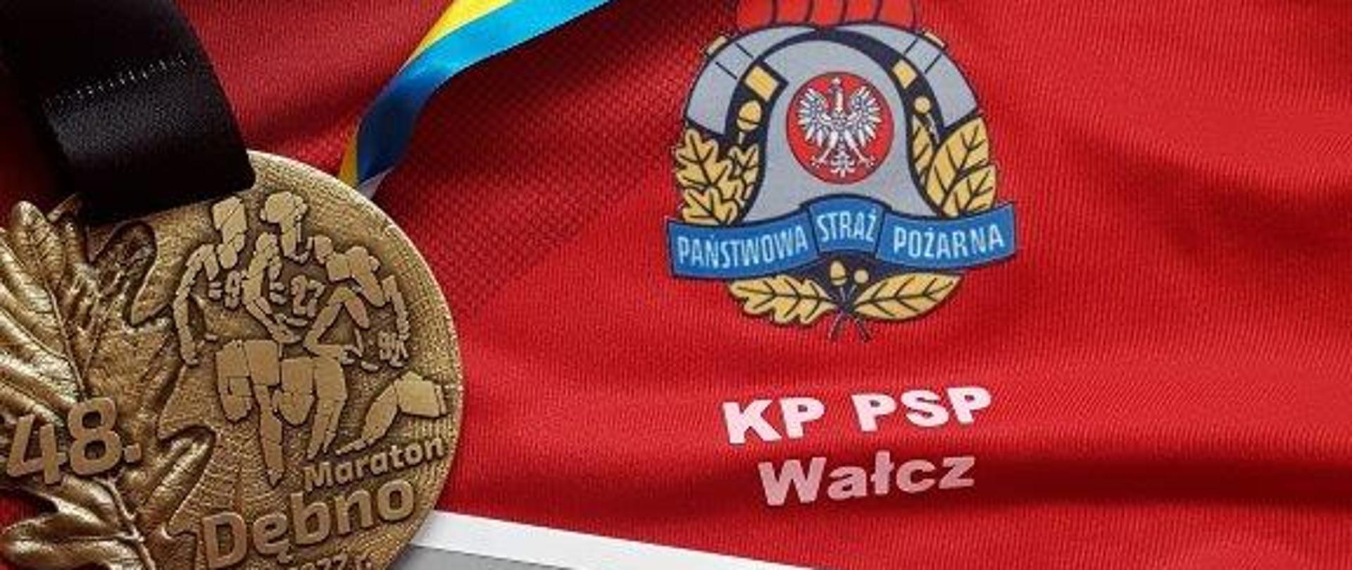 Zdjęcie przedstawia medal, numer startowy Maratonu w Dębnie na tle sportowej koszulki z logo PSP i KP PSP Wałcz
