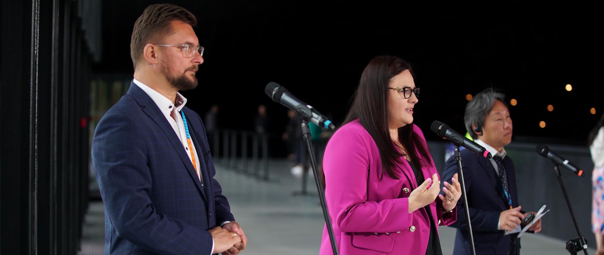 Na zdjęciu wiceminister Małgorzata Jarosińska-Jedynak w różowej marynarce przemawiające w trakcie konferencji prasowej. Po prawej przedstawiciel UN-Habitat Neil Khor, po prawej prezydent Katowci Marcin Krupa. Przed przemawiającymi stoją mikrofony. 