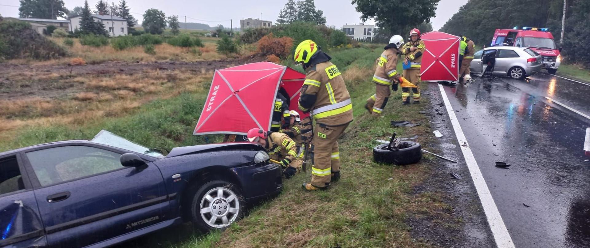 Dzień, opady deszczu, uszkodzone dwa samochody osobowe, strażacy prowadzący działania