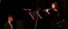 Zdjęcie przedstawia flecistkę i absolwentkę szkoły Celestynę Łuczak występującą na scenie w towarzystwie Pana Tomasza Ratajczaka przy fortepianie.