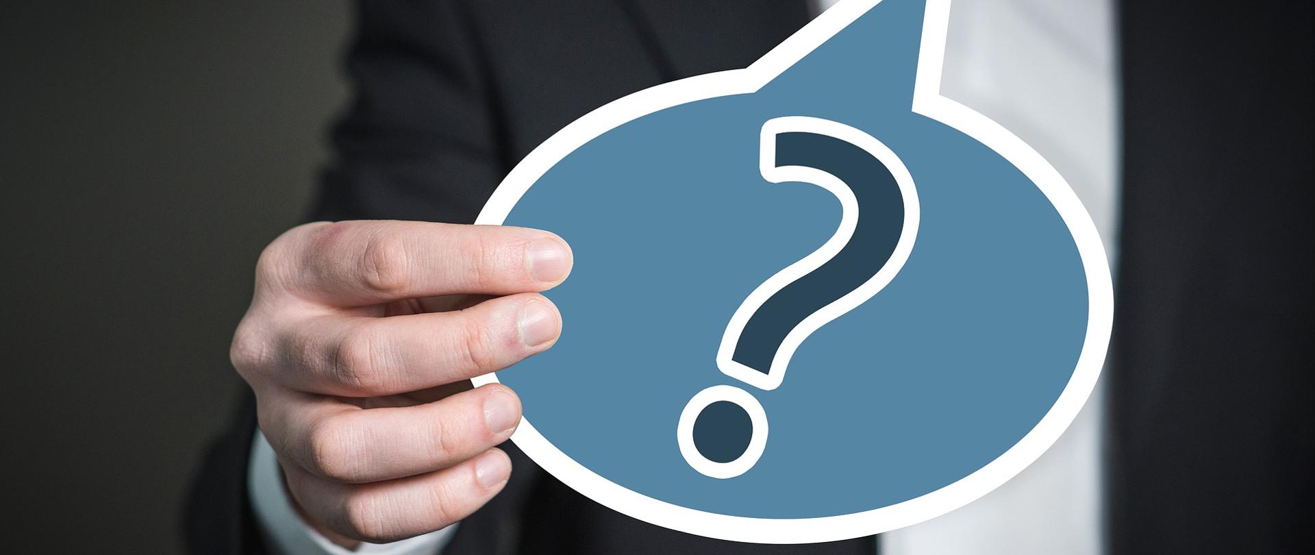 postać trzymająca tabliczkę ze znakiem zapytania.