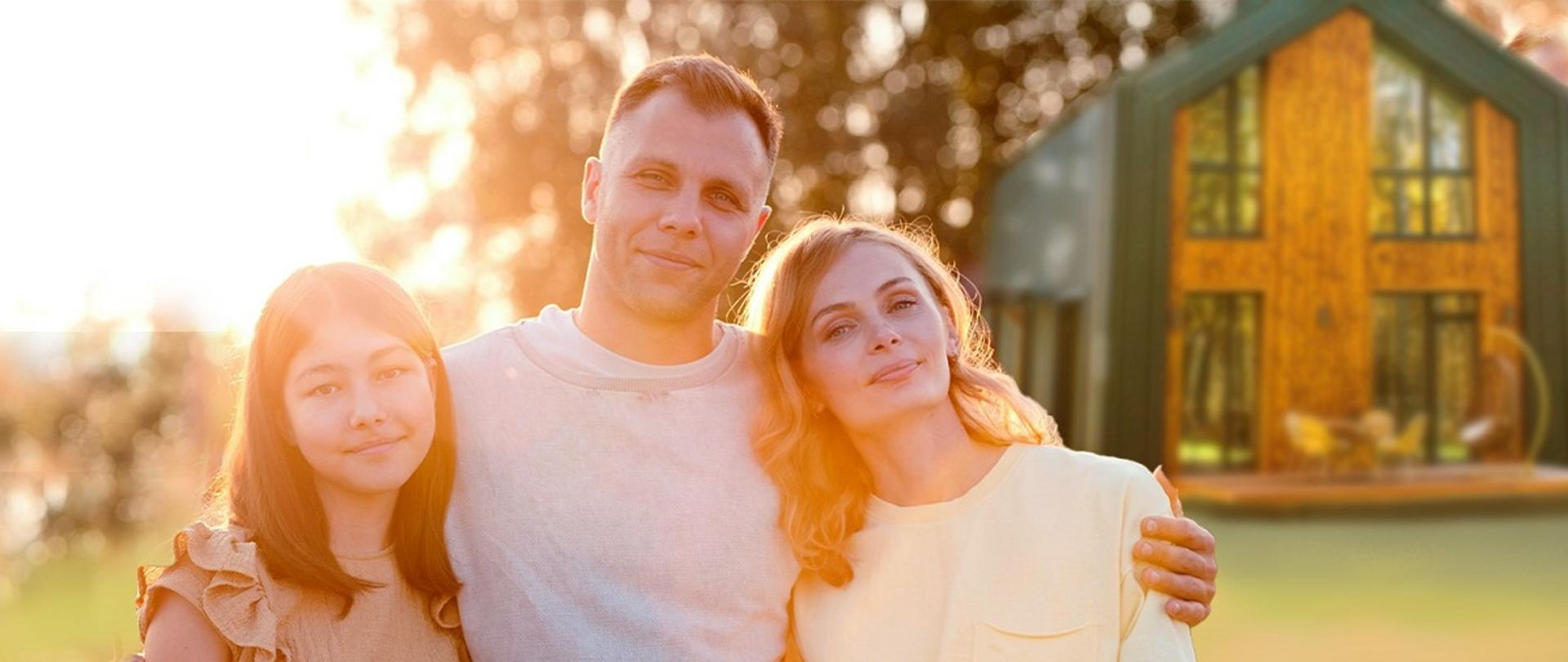 Kobieta, mężczyzna i dziewczynka stoją przytuleni przez domem