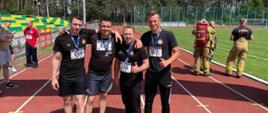Zdjęcie przedstawia strażaków w trakcie zawodów sportowych.
W tle stadion sportowy.
