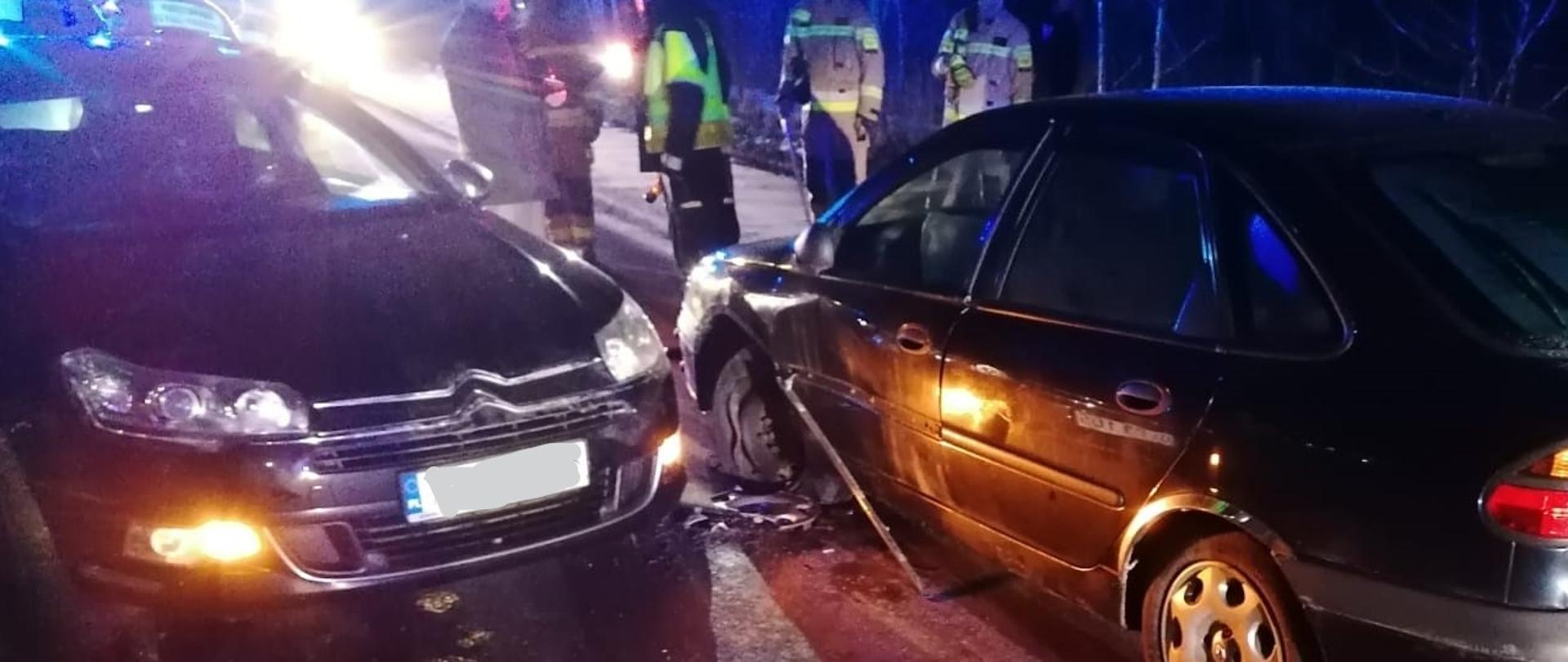Na zdjęciu widzimy dwa zniszczone w wyniku kolizji auta osobowe. Na dalszym planie widać przedstawicieli służb ratowniczych.