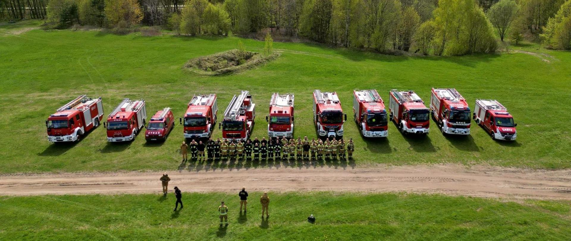 Druhowie stoja na zbiurce przed pojazdami na placu 