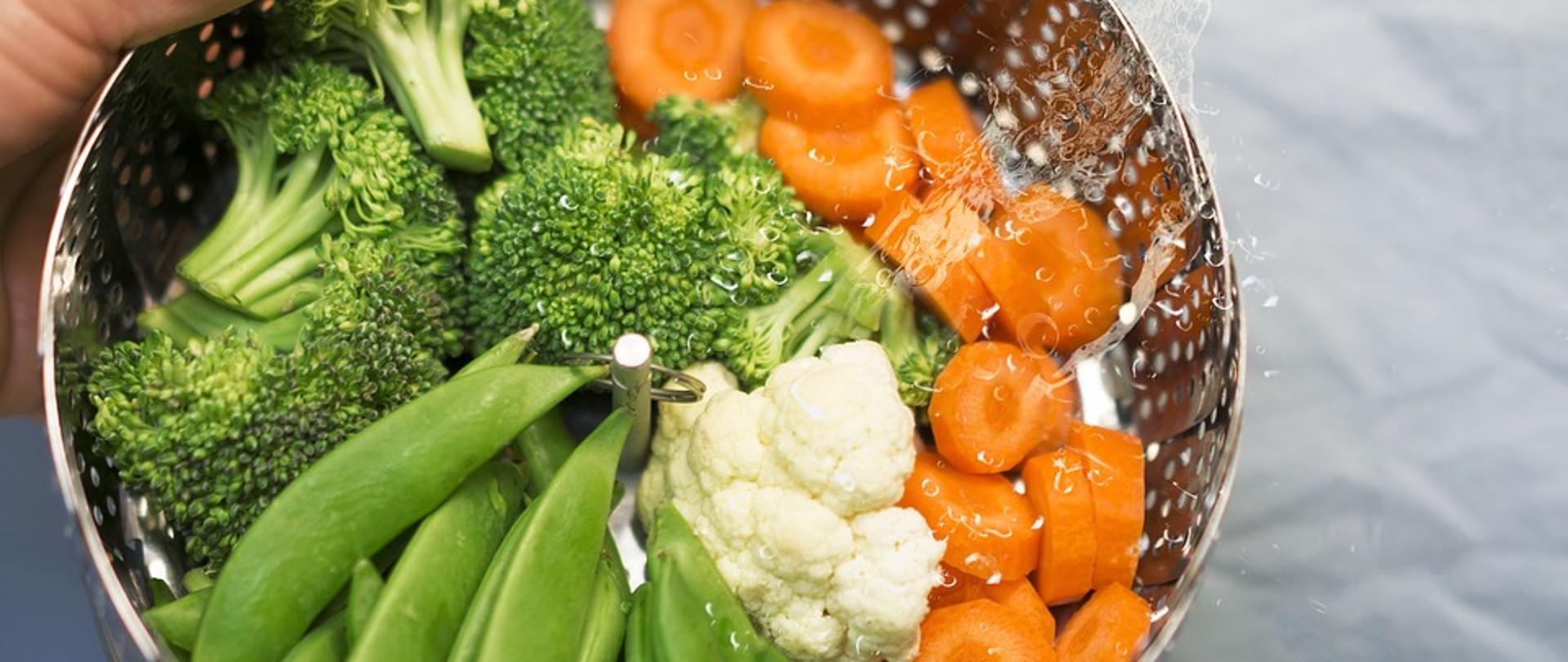 Koszyk z umytymi warzywami, zielone różyczki brokuła, pomarańczowe plasterki marchewki, białe różyczki kalafiora i zielone strąki fasoli