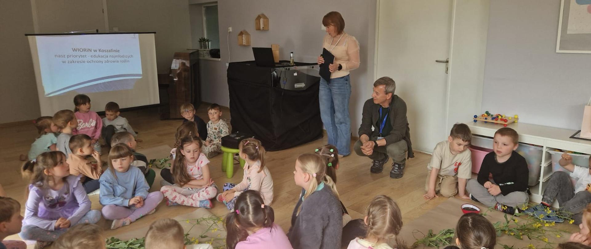 Zdjęcie przedstawia salę wypełnioną dziećmi w wieku przedszkolnym. Dzieci siedzą na podłodze i słuchają wykładu inspektorów WIORiN w Szczecinku.