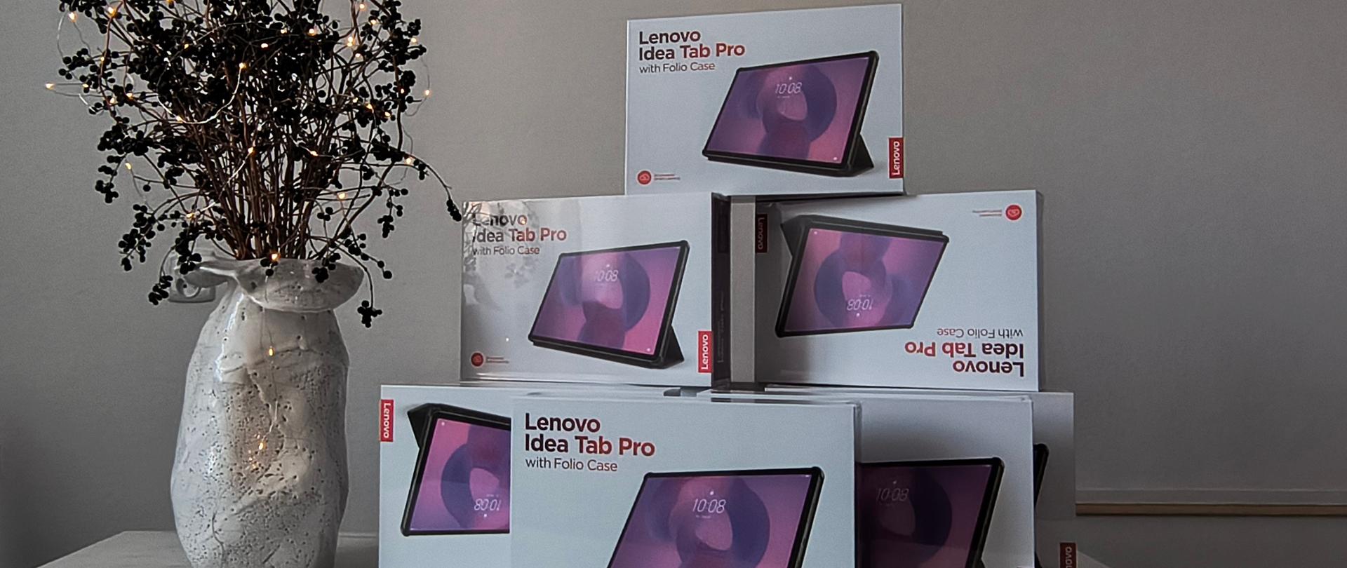 zdjęcie przedstawia ustawione na stole tablety, obok stoi wazon ze stroikiem świątecznym
