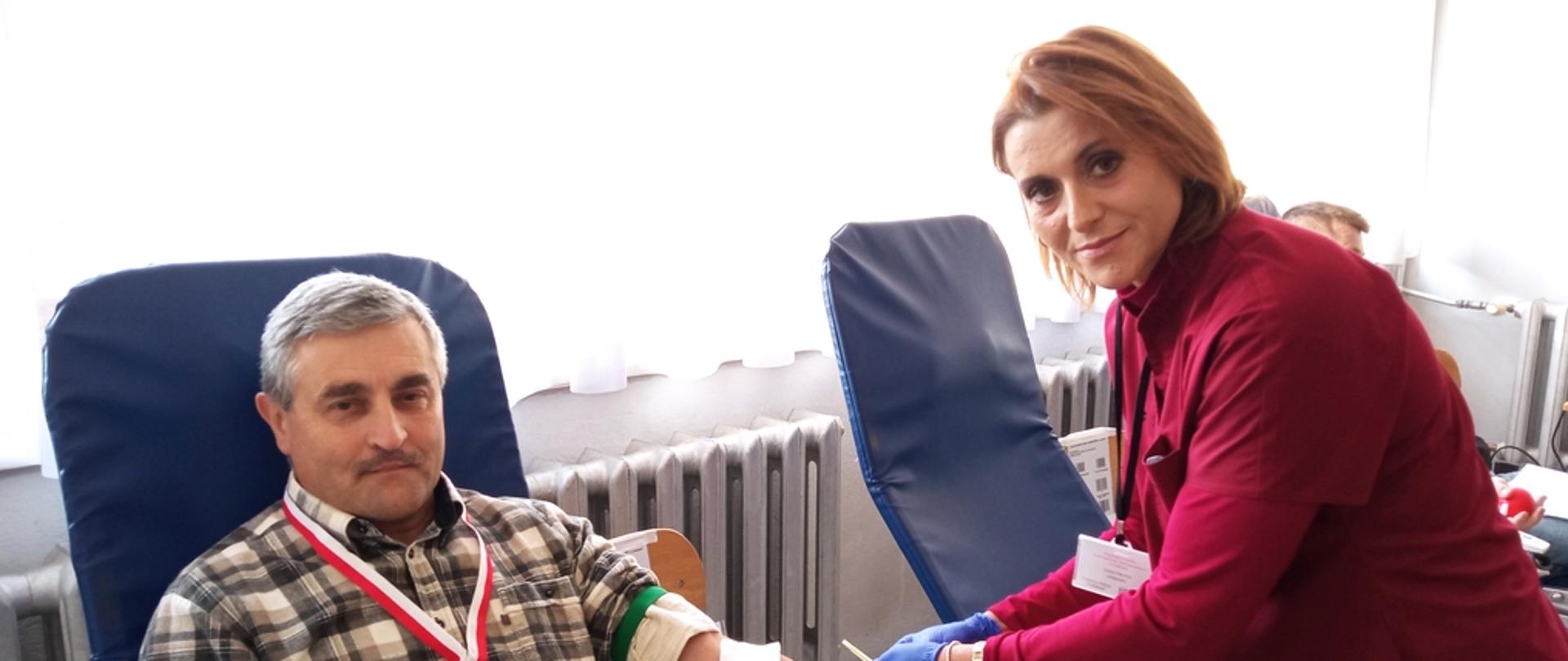 Na zajęciu widoczny mężczyzna siedzący na fotelu na sali oddający krew podczas akcji zbiórki krwi zorganizowanej przez Kluby Honorowych Dawców Krwi Polskiego Czerwonego Krzyża przy Komendzie Powiatowej Państwowej Straży Pożarnej w Gorlicach i Klub Honorowych Dawców Krwi Polskiego Czerwonego Krzyża Moszczenica 