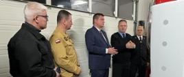 Zdjęcie wykonane w remizie OSP Tuchorza. NA zdjęciu widoczne pięć osób. Od lewej Wójt Gminy Siedlec, Komendant Powiatowy PSP w Wolsztynie, Poseł na Sejm RP Marcin Porzucek oraz dwóch strażaków ochotników.