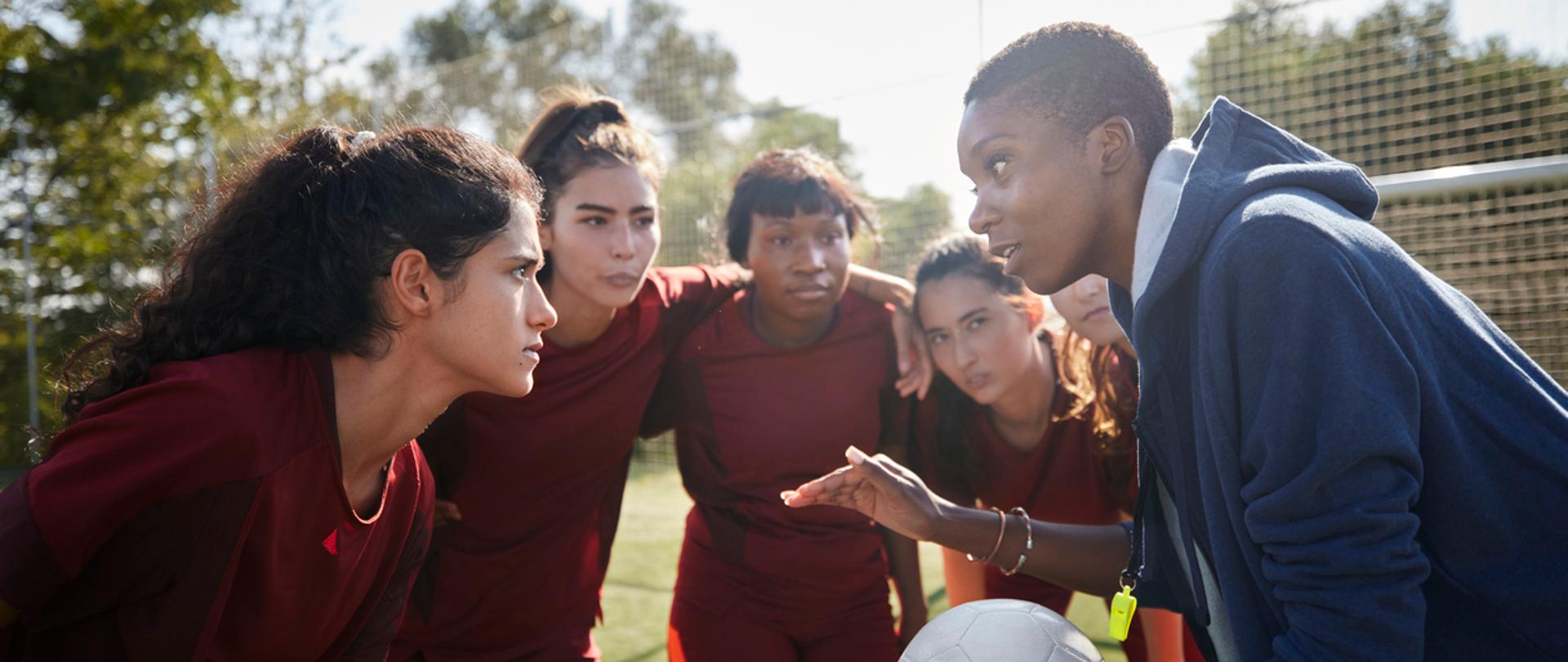 Group of female soccer players listening to their african-american female coach before game