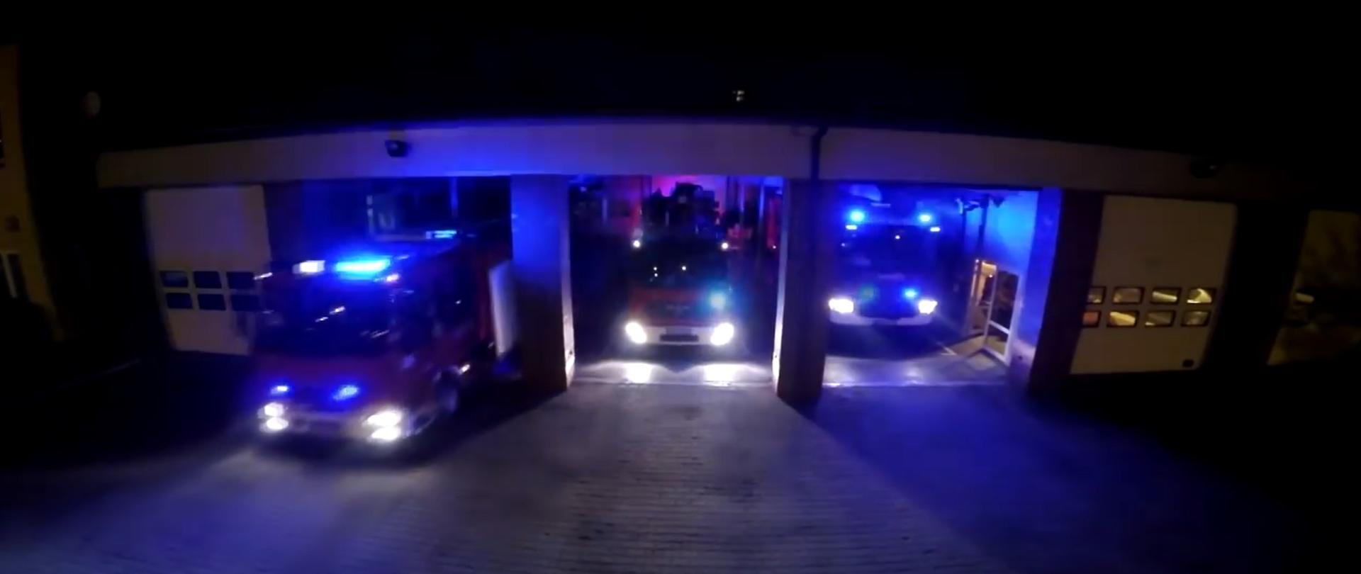 Zdjęcie przedstawia wyjeżdżające zastępy z Komendy Miejskiej Państwowej Straży Pożarnej w Świętochłowicach. Zdjęcie wykonane w porze nocnej. Samochody pożarnicze mają włączone niebieskie światła alarmowe.