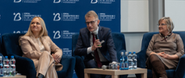 Debata poświęcona nowoczesnym standardom leczenia udarów . Paneliści siedzą w fotelach na scenie, dyskutując o rozwoju trombektomii w Bydgoszczy. W tle widoczna ścianka szpitala uniwersyteckiego nr 2 w Bydgoszczy. 