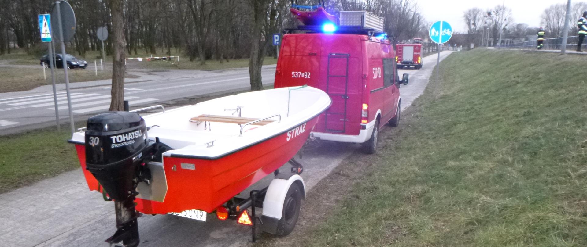 łódź strażacka oraz pojaz pożarniczy stojący na drodze