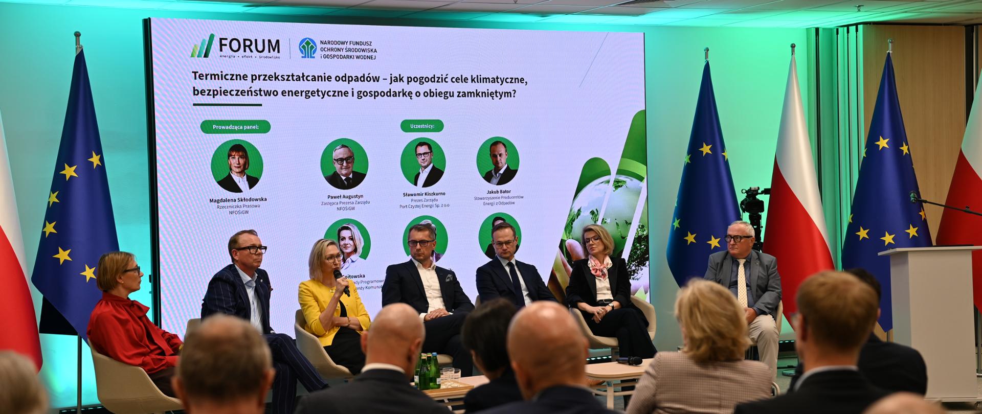 7 prelegentów siedzi na tle ekranu z wyświetlonymi ich zdjęciami. Obok flagi Polski i UE.
