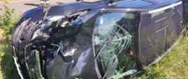 Zdjęcie przedstawia wypadek samochodu osobowego oraz skutera. Rozbity samochód leży na skuterze w rowie