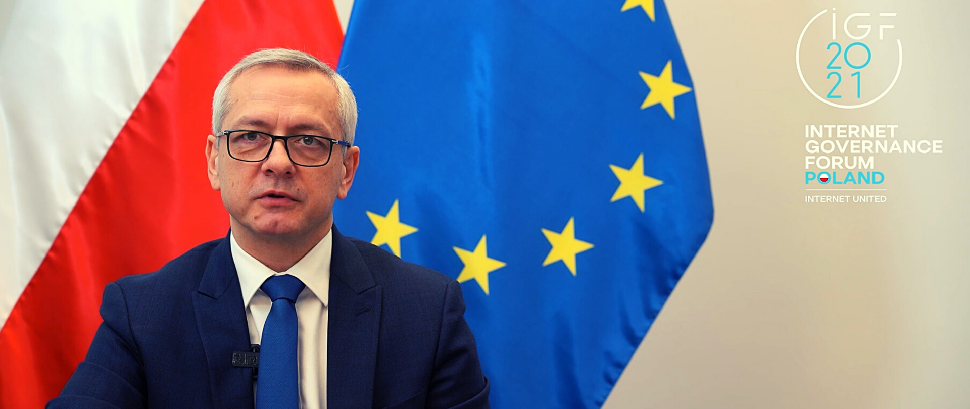 Minister Marek Zagórski podczas wystąpienia. Za nim flagi Polski i Unii Europejskiej. Z prawej strony - logo IGF 2021 i tekst: Internet Governance Forum Poland | Internet United.