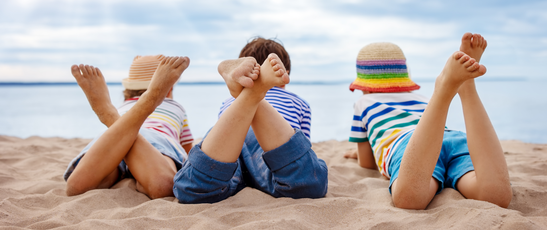 Zdjęcie przedstawia troje dzieci leżących na plaży z założonymi nogami.