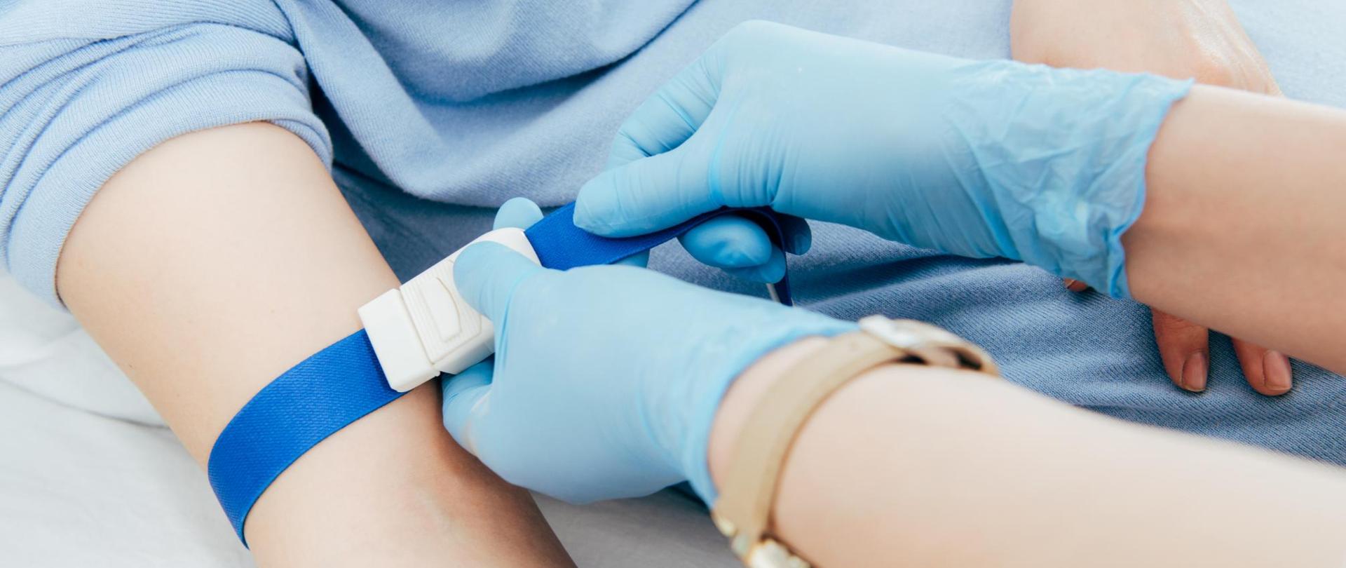 Na zdjęciu jest widoczna ręka pacjenta, na której lekarz zaciska opaskę.