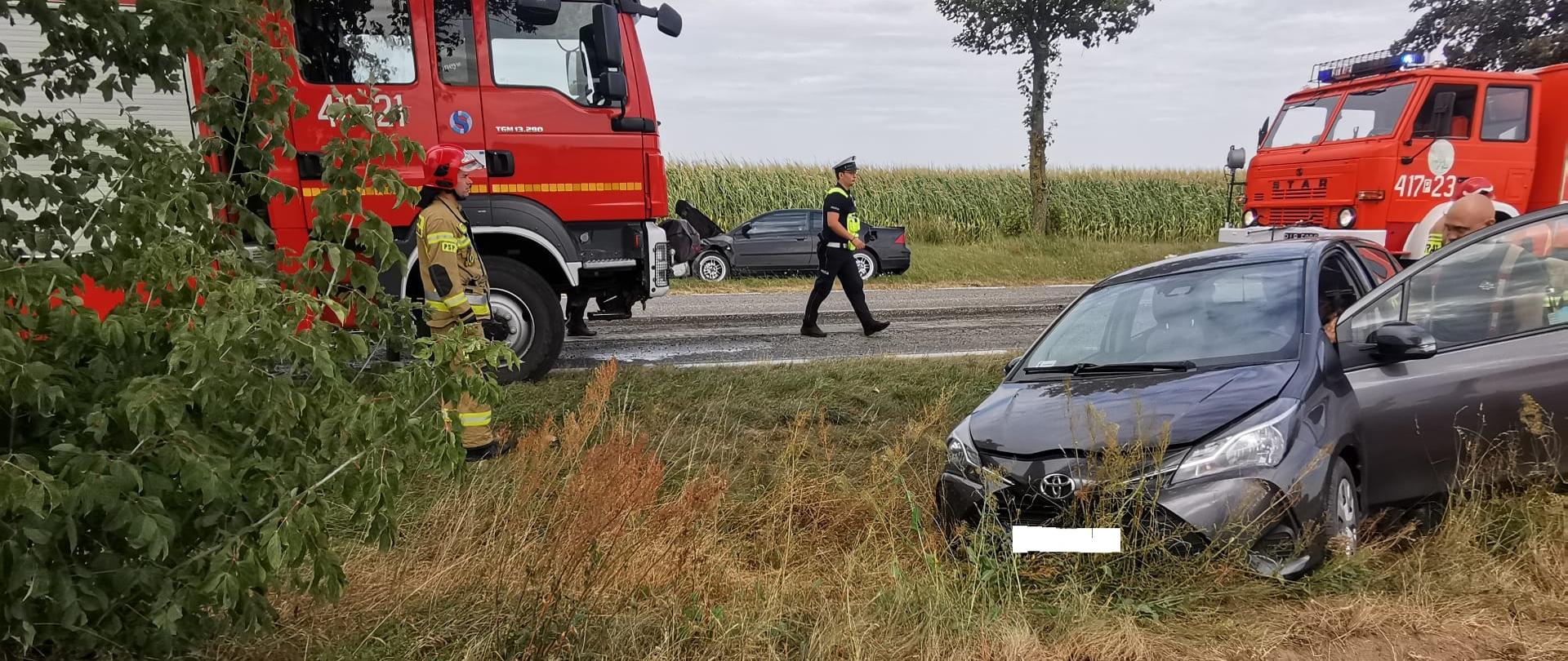Samochód osobowy Toyota w rowie po zdarzeniu drogowym, na miejscu strażacy i policja.