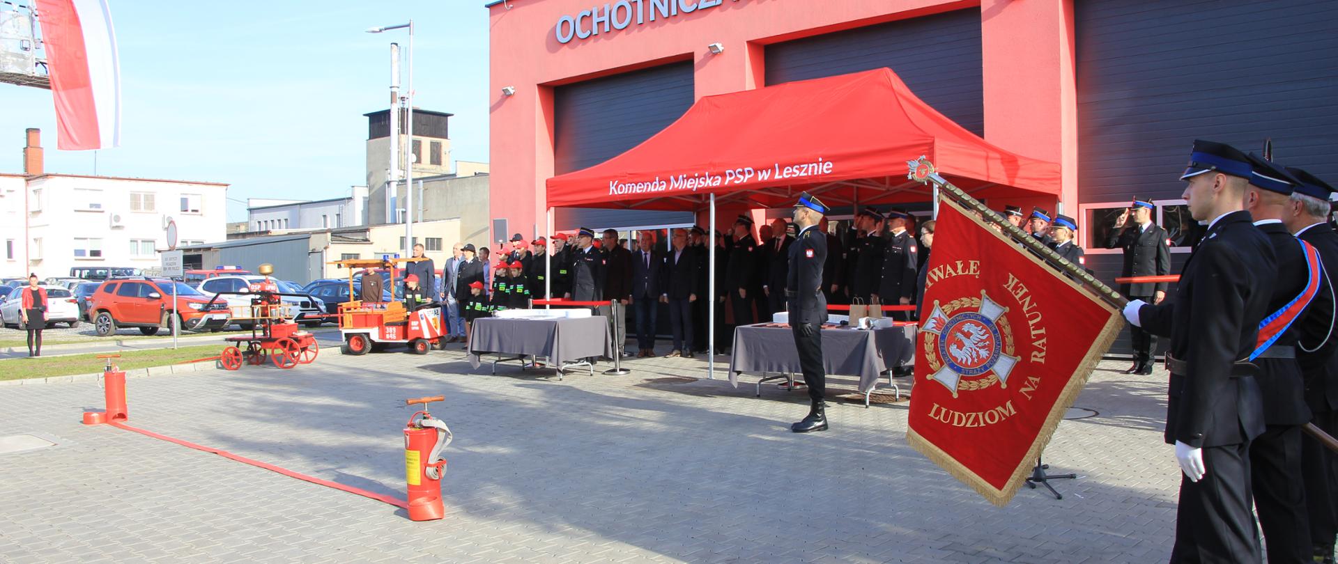 Strażacy i osoby cywilne stoją w szeregu pod namiotem.
